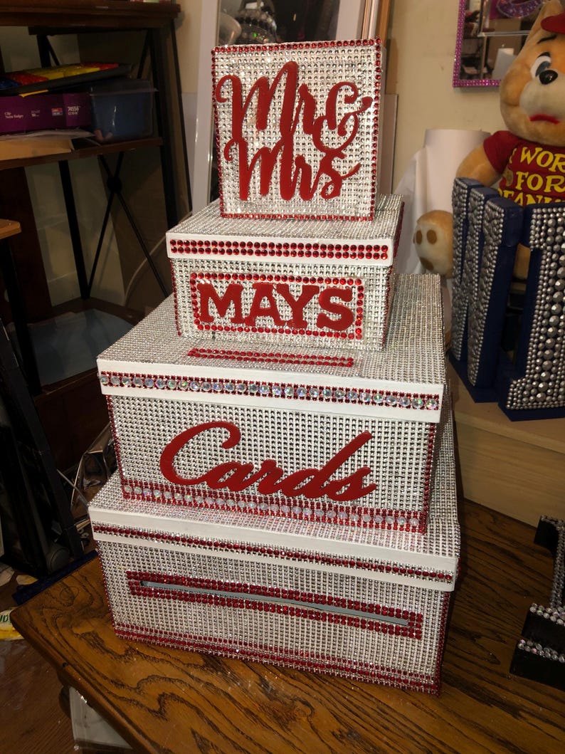 Puede incluir: Un conjunto de cajas decorativas, ideal para una boda o evento especial. Las cajas blancas est&aacute;n cubiertas de pedrer&iacute;a plateada, con detalles rojos y letras que dicen "Mr & Mrs", "Mays" y "Cards".