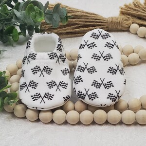 May include: A pair of white baby booties with a black checkered flag pattern.
