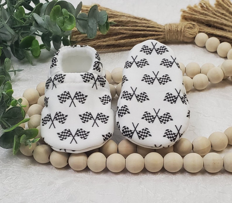 May include: A pair of white baby booties with a black checkered flag pattern.