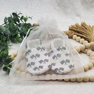 May include: A pair of white baby booties with a checkered flag pattern. The booties are in a white organza bag.