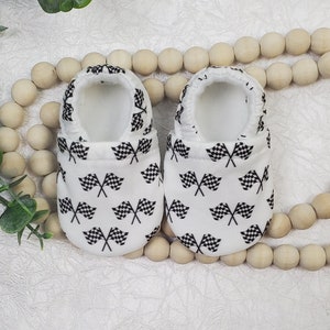 May include: A pair of white baby booties with a black and white checkered flag pattern.
