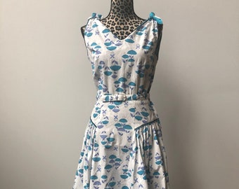 May include: A white sleeveless dress with a blue and purple floral print. The dress has a V-neckline, a belt, and a full skirt.