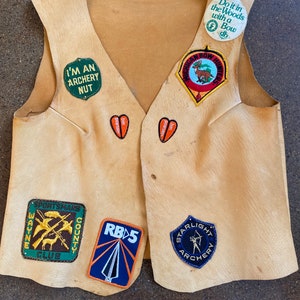 May include: A tan leather vest with various patches, including "I'm an Archery Nut", "Sportsmans Wayne County Club", "RB5", "Starlight Archery", "Michigan Bow Hunters", and "Do it in the Woods with a Bow".