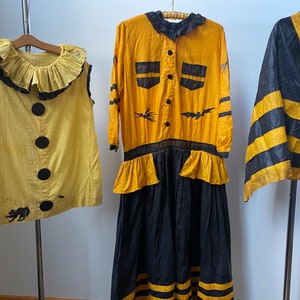May include: Three vintage Halloween costumes: a yellow and black clown costume, a yellow and black witch costume with a long skirt, and a yellow and black cape.