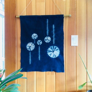 May include: A dark blue fabric wall hanging with a white tie-dye design of circles. The hanging is attached to a wooden dowel rod with string.