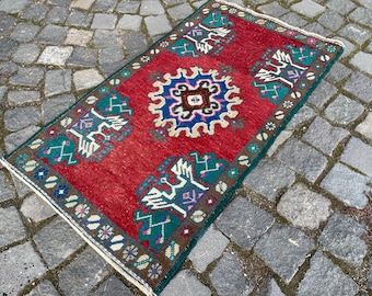 May include: A rectangular area rug featuring a vibrant red background with a central blue and white geometric medallion. The rug is decorated with green and white stylized bird motifs and a dark brown border with small floral patterns.