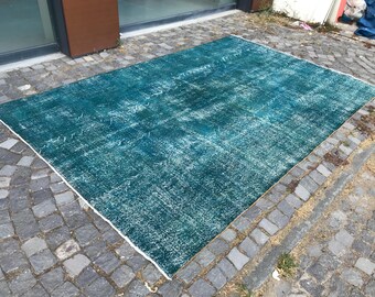 May include: A rectangular, distressed teal rug with a white border. The rug has a faded, vintage appearance with white accents throughout. The rug is placed on a cobblestone surface, suggesting an outdoor setting. The rug's color is a deep teal, with lighter areas creating a worn effect.