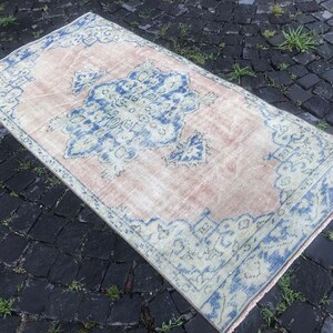 May include: Rectangular vintage rug with a faded pink central field and a detailed blue and off-white border. The rug features a central medallion design in blue and off-white, adding a touch of elegance. The rug's dimensions are approximately 3 x 5 feet.