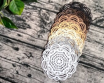 May include: A set of six decorative paper doilies in various shades of brown, gray, and white. The doilies are layered on top of each other and have a delicate, intricate design.