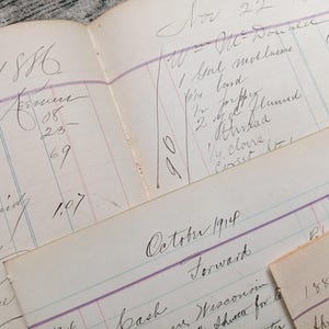 May include: A close-up of a vintage ledger with handwritten entries in black ink. The ledger is open to the year 1886 and includes entries for November 22 and October 1914. The ledger is on a textured surface.