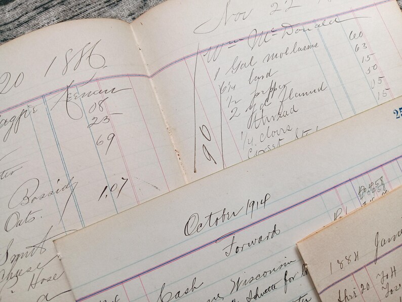 May include: A close-up of a vintage ledger with handwritten entries in black ink. The ledger is open to the year 1886 and includes entries for November 22 and October 1914. The ledger is on a textured surface.