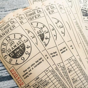 May include: A collection of vintage beige paper transit transfer tickets from Citizens Transit Co. Each ticket features a circular clock graphic with numbers 1 through 12, the text 15 A.M. 45 and 15 P.M. 45, and a red serial number 220102 printed on the front.