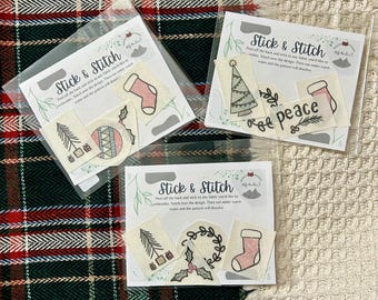 May include: Three packages of "Stick & Stitch" embroidery patterns. Each package contains several small, festive designs, including a Christmas tree, a sock, and the word "peace". The patterns are on a cream-colored background.