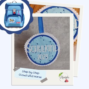 Könnte beinhalten: Blau-weißer gestickter Aufnäher mit dem Text "Schulkind 2023" in Weiß. Der Aufnäher ist an einem blauen Band befestigt.