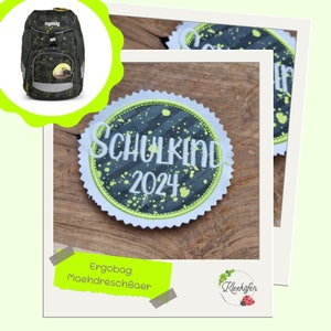 Könnte beinhalten: Ein runder, grau-grüner gestickter Aufnäher mit weißen Nähten. Der Aufnäher trägt die Aufschrift "Schulkind 2024" mit einem kleinen Herzsymbol.