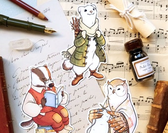 Op de afbeelding: Drie geïllustreerde dieren stickers met een das die een boek leest, een wezel die een geruit jasje en een witte sjaal draagt, en een uil die een witte bol wol breit. De stickers zijn op een achtergrond van oud papier met muzieknoten en een handgeschreven notitie.