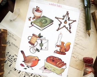 May include: A sheet of stickers with a winter theme. The stickers feature illustrations of a cup of hot chocolate, a book, a star, a squirrel, a robin, a spool of thread, a letter, a loaf of bread, and a candle. The stickers are printed on white paper and have a matte finish.