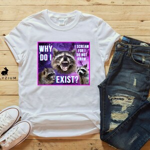 May include: White t-shirt with a graphic of three raccoons against a purple galaxy background. The text on the graphic reads "Why do I exist?" and "I scream for I do not know".