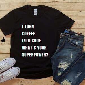K&ouml;nnte beinhalten: Schwarzes T-Shirt mit wei&szlig;em Text, der "I turn coffee into code. What's your superpower?" lautet. Der Text hat einen Glitch-Effekt.