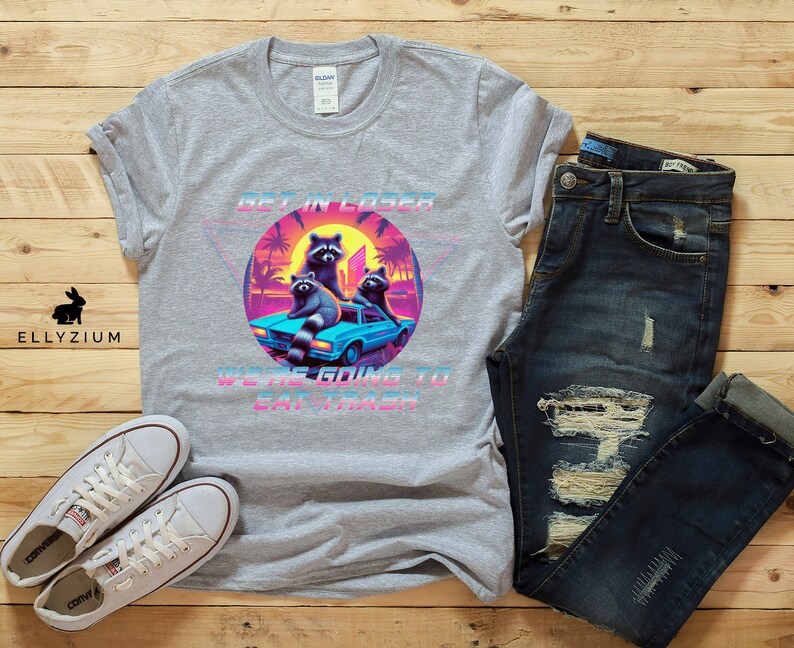 May include: A gray t-shirt with a retro-style graphic of raccoons in a car. The graphic says "Get in Loser, We're Going to Eat Trash".