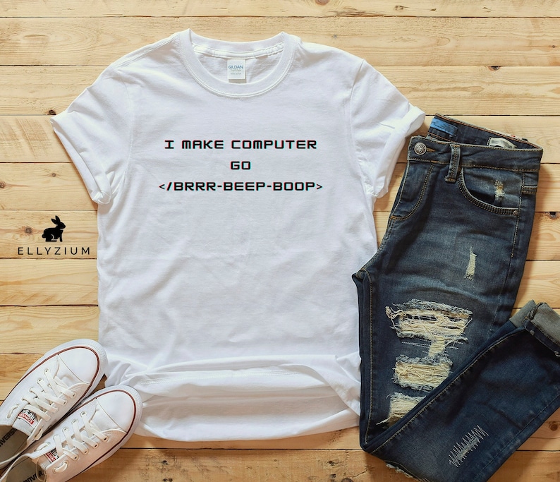 May include: White t-shirt with the text "I make computer go <brr-beep-boop>" printed on it. The t-shirt is laid out on a wooden surface with a pair of blue jeans and a pair of white trainers.