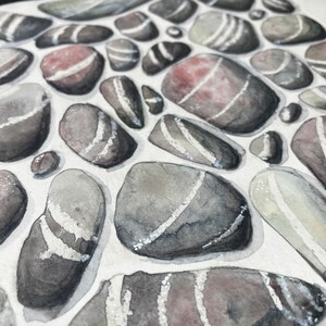 May include: Watercolor painting of smooth, gray and white stones with a few pink stones. The stones are painted in a realistic style with subtle details.