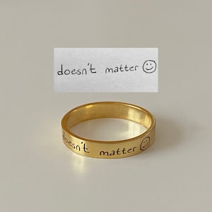 May include: Gold band ring with the inscription "doesn't matter" and a smiley face.