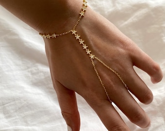 May include: A gold chain bracelet with a star design. The bracelet has a long chain that extends to the finger, creating a finger chain effect.