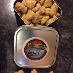 May include: A silver tin filled with maple sugar candies in the shapes of hearts and maple leaves. The tin has a label that reads "Covered Bridge Sugaring".