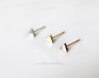 May include: Three triangle shaped stud earrings in silver, gold, and rose gold.