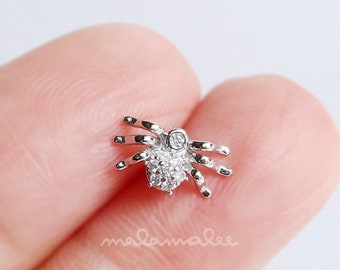 May include: A silver spider charm with clear crystal accents. The spider is detailed with eight legs and a round body.
