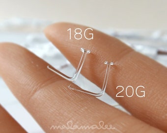 May include: Two clear nose rings, one labeled 18G and the other 20G, are shown on a finger.