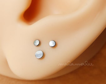 May include: Three small, silver, round stud earrings in a person's ear.