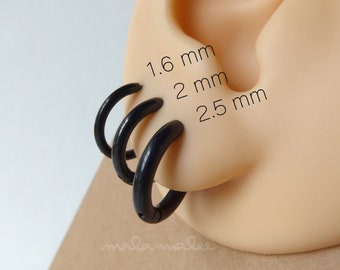 May include: Three black hoop earrings in different sizes: 1.6 mm, 2 mm, and 2.5 mm. The earrings are shown on a model ear.