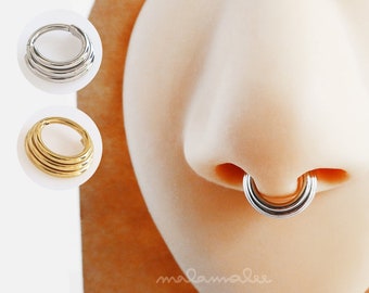 May include: A close-up of a nose piercing with a silver ring. The ring is made of multiple bands and is worn in the septum.