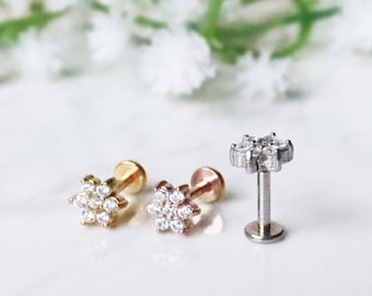 May include: Three small flower-shaped earrings with clear cubic zirconia stones. The earrings are in gold, rose gold, and silver.