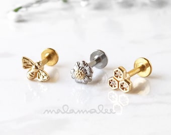 May include: Three gold body jewelry pieces: a bee, a flower, and a honeycomb design. Each piece is on a silver post.