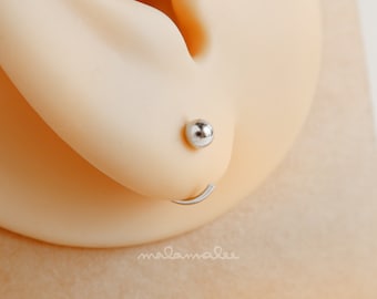 May include: A close-up of a silver hoop earring with a small silver ball at the end. The earring is in a person's earlobe.