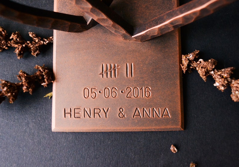 K&ouml;nnte beinhalten: Eine kupferfarbene Metallskulptur mit einem rechteckigen Sockel. Der Sockel ist mit dem Text "IIII II 05.06.2016 HENRY & ANNA" graviert.