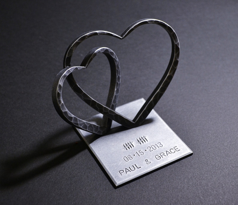 May include: Two interlocking metal hearts on a silver base with the inscription "06.15.2013 PAUL & GRACE".