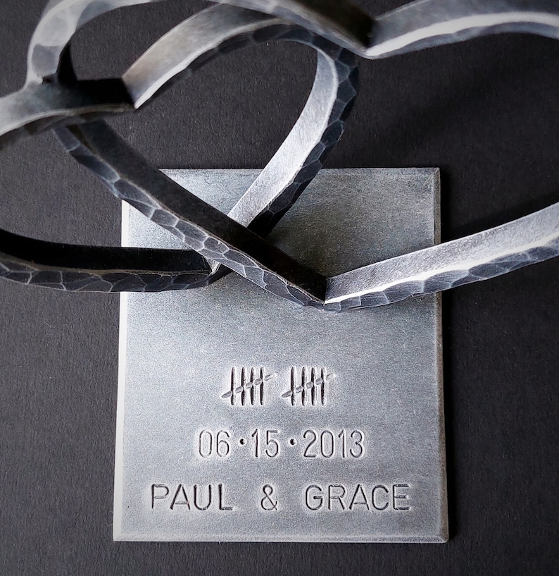 May include: Two intertwined metal hearts on a silver square base with the date 06.15.2013 and the names Paul & Grace engraved.