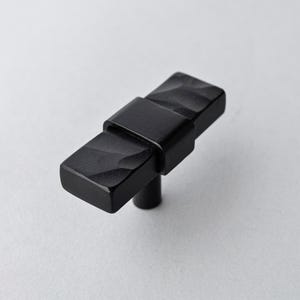 May include: A black cabinet knob with a rectangular shape and a textured surface. The knob has a central band and a stem for mounting. The hardware is made of metal and is suitable for furniture or cabinetry.