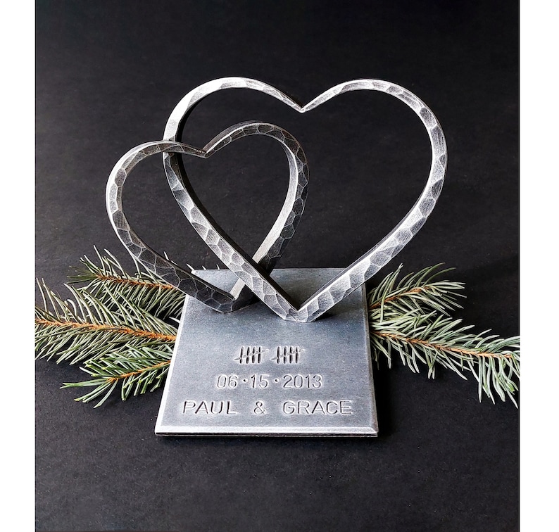 May include: A silver metal sculpture of two intertwined hearts on a square base. The base is engraved with the date "06.15.2013" and the names "PAUL & GRACE".