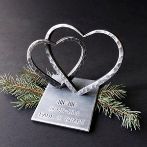 May include: Two interlocking metal hearts on a silver base with the date "06.15.2013" and the names "PAUL & GRACE" engraved.