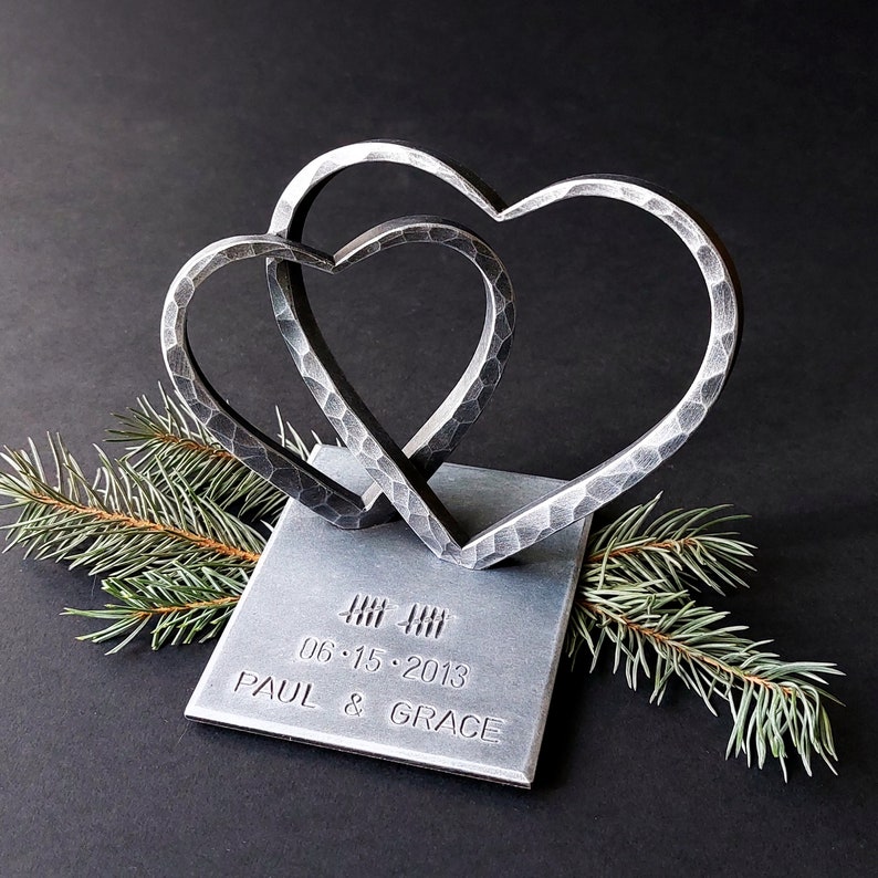 May include: Two interlocking metal hearts on a silver base with the date "06.15.2013" and the names "PAUL & GRACE" engraved.
