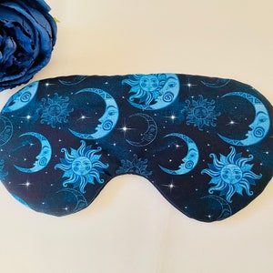 May include: A blue sleep mask with a pattern of moons and suns on a black background. The mask has a small tag that says "The Sleep".