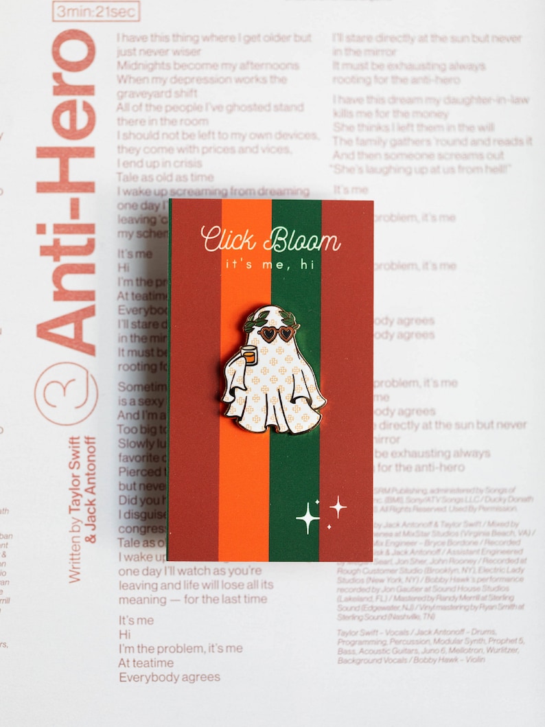 May include: A white enamel pin with a ghost wearing sunglasses and holding a cup. The ghost has a green wreath around its head. The pin has a red, orange, and green striped background with the text "Click Bloom it's me, hi".