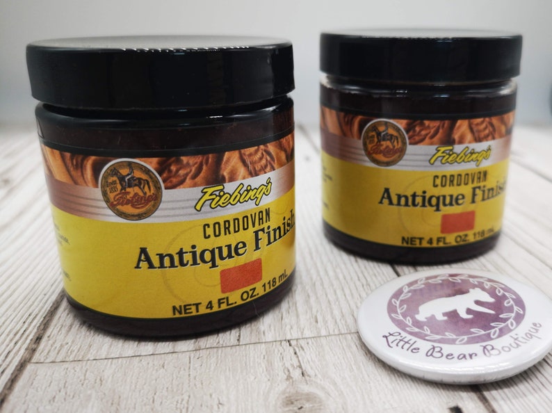 May include: Two 4-ounce bottles of Fiebing's Cordovan Antique Finish leather dye. The bottles are yellow with brown text and a brown leather design. The bottles are sitting on a white wooden surface.
