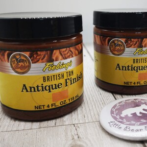 May include: Two brown glass jars with black lids containing Fiebings British Tan Antique Finish leather dye. Each jar contains 118 ml of dye.