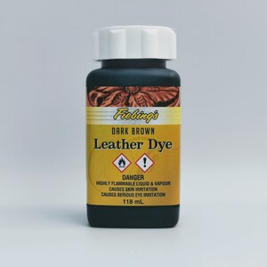 May include: A bottle of Fiebing's Dark Brown Leather Dye. The bottle is black with a white lid and a yellow label with a warning symbol. The label reads "DANGER: HIGHLY FLAMMABLE LIQUID & VAPOUR CAUSES SKIN IRRITATION CAUSES SERIOUS EYE IRRITATION 118 mL."